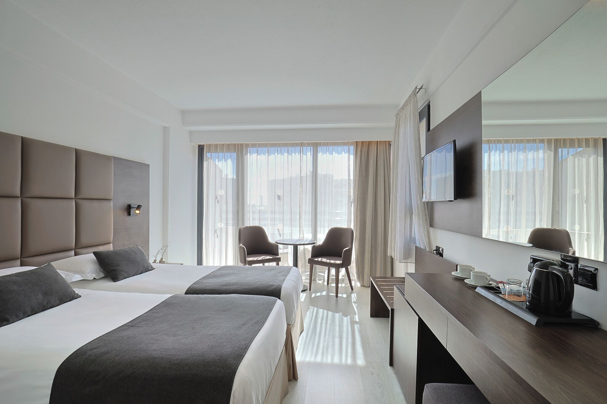 Een hotelkamer met twee bedden, een bureau, een televisie en een raam met gordijnen.