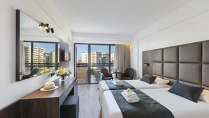Habitación de hotel moderna con dos camas, un escritorio, un espejo y vistas a la ciudad.
