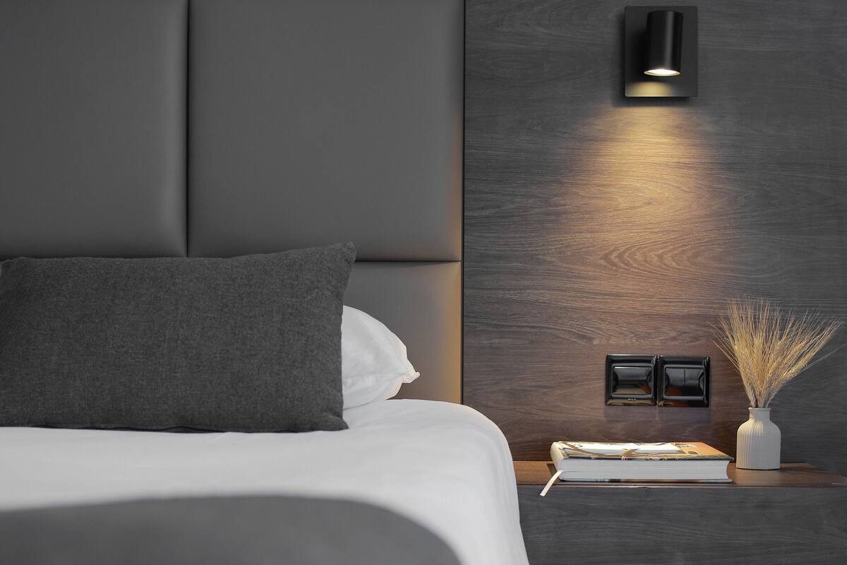Ein modernes Schlafzimmer mit einem großen Bett, einem Nachttisch mit Lampe und einer Wandleuchte.