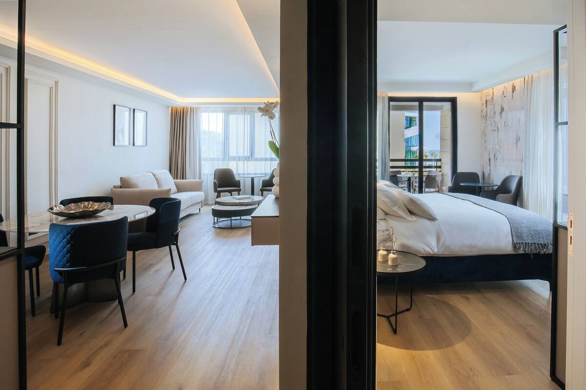 Ein modernes Hotelzimmer mit einem Bett, einer Sitzecke mit Tisch und Stühlen und Blick auf die Stadt.