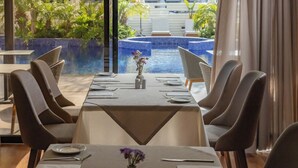 Comedor con una mesa dispuesta para cuatro personas, con vistas a una piscina y abundante vegetación.