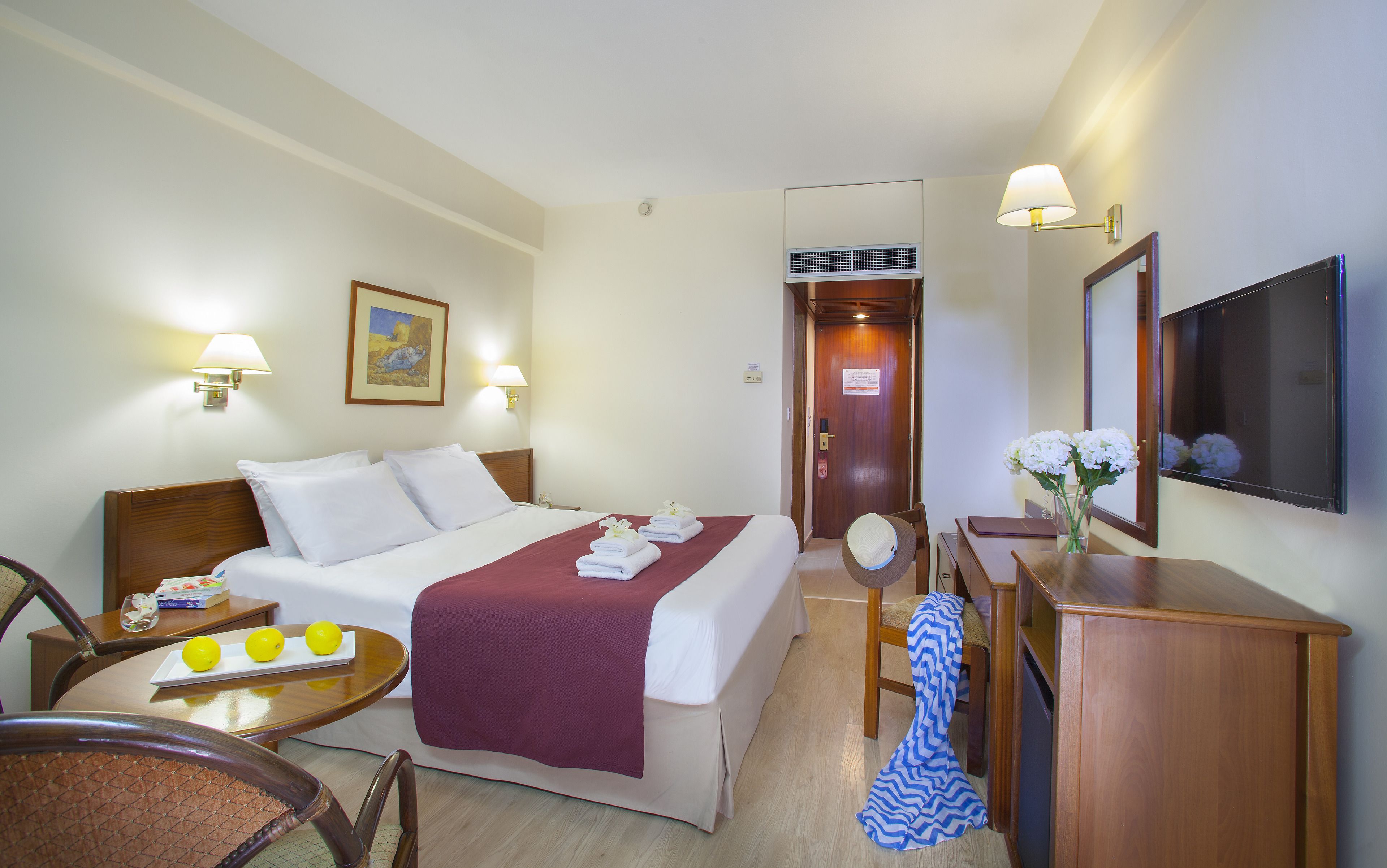 A hotel room with a bed, bedside table, chair, desk, TV, and a door leading to another room.