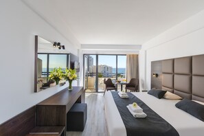 Habitación de hotel moderna con una cama grande, un escritorio, una silla y un balcón con vistas a la ciudad.