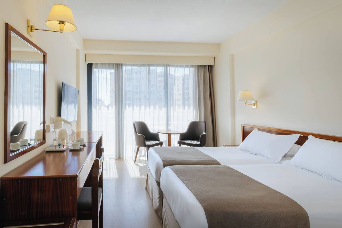 Ein Hotelzimmer mit zwei Betten, einem Schreibtisch, einem Telefon, einem Sessel und einem Fernseher.