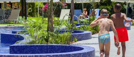 A pool area with tiled steps and a mosaic design, surrounded by greenery and umbrellas.