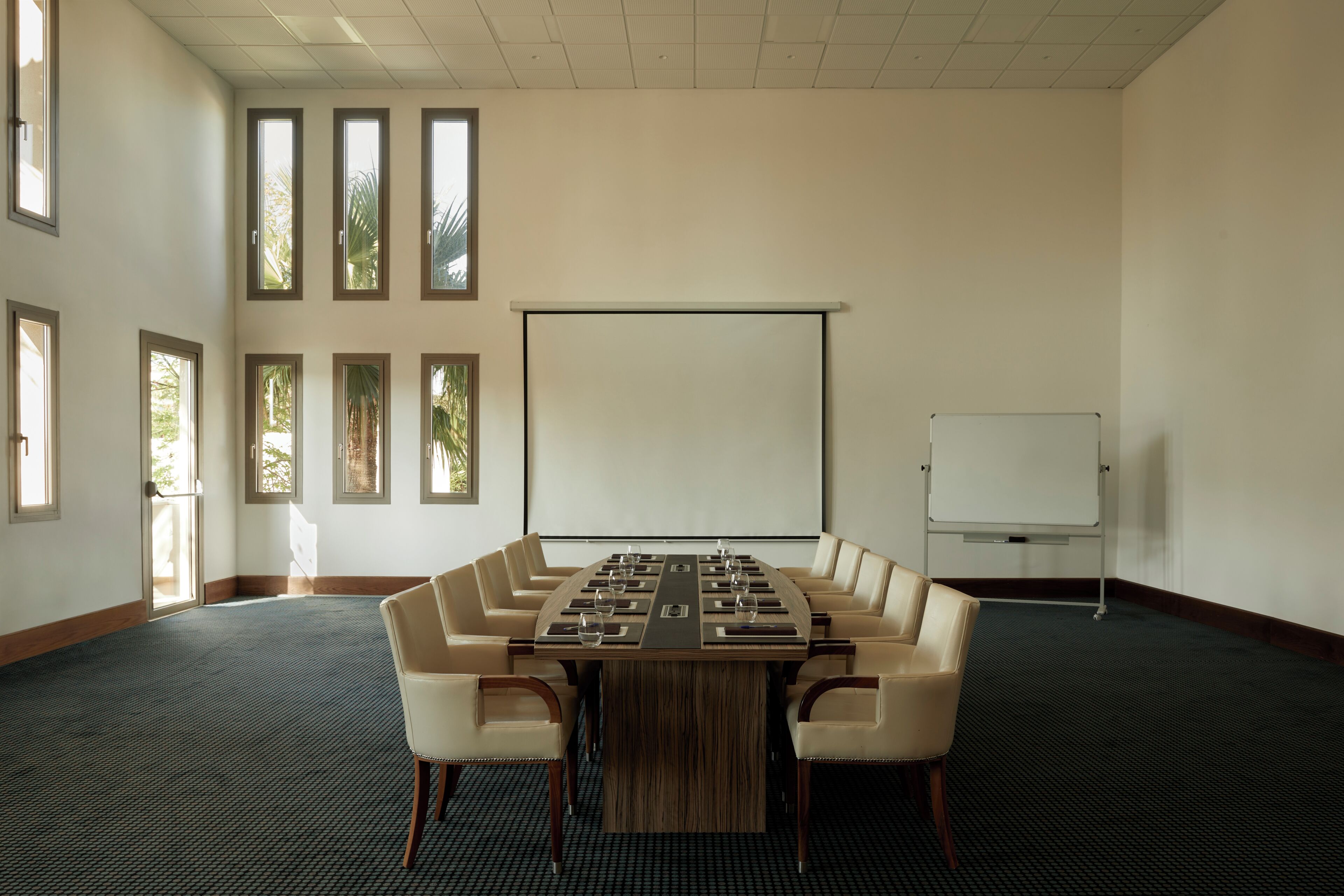 Uma sala de conferências com uma mesa comprida, várias cadeiras, uma tela de projetor e um quadro branco.
