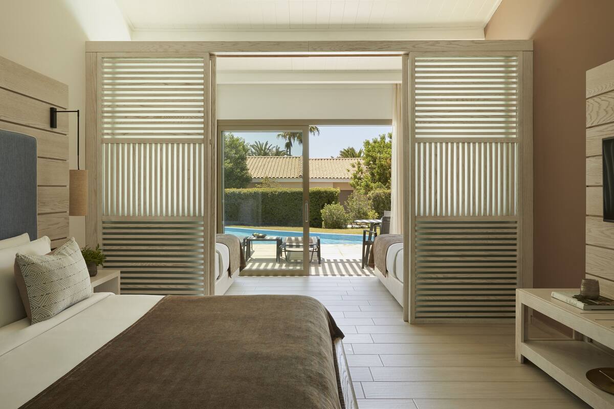 Een slaapkamer met een bed, een televisie en uitzicht op een zwembad en een terras.