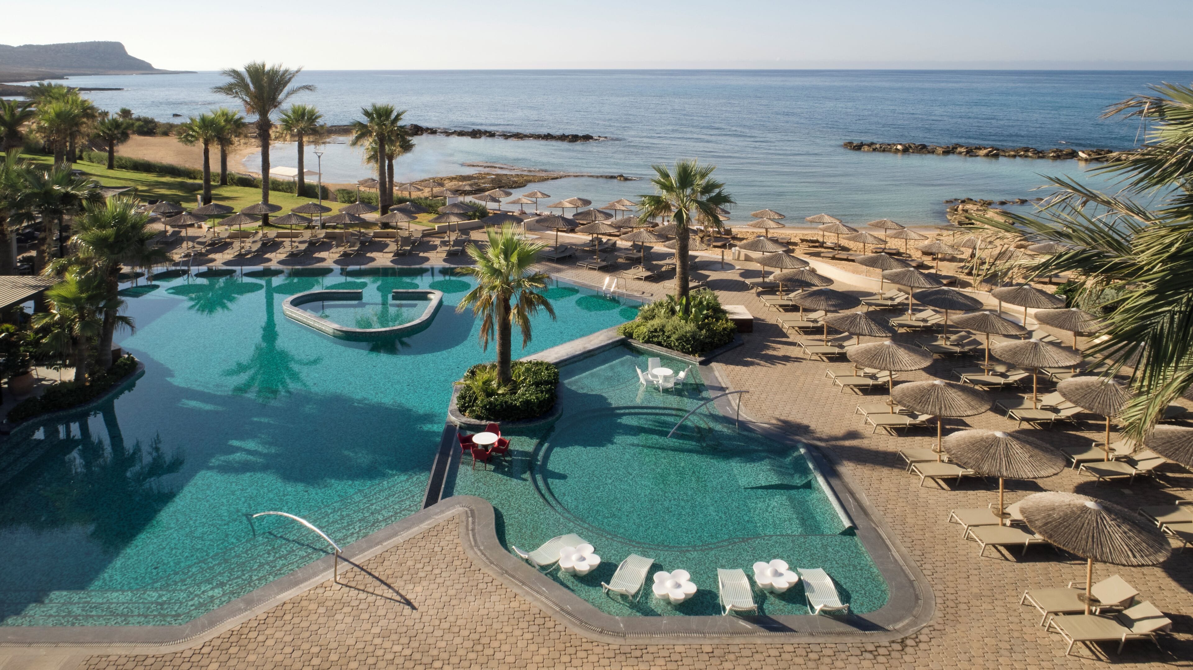 Un resort con una grande piscina, lettini, ombrelloni e vista sul mare.