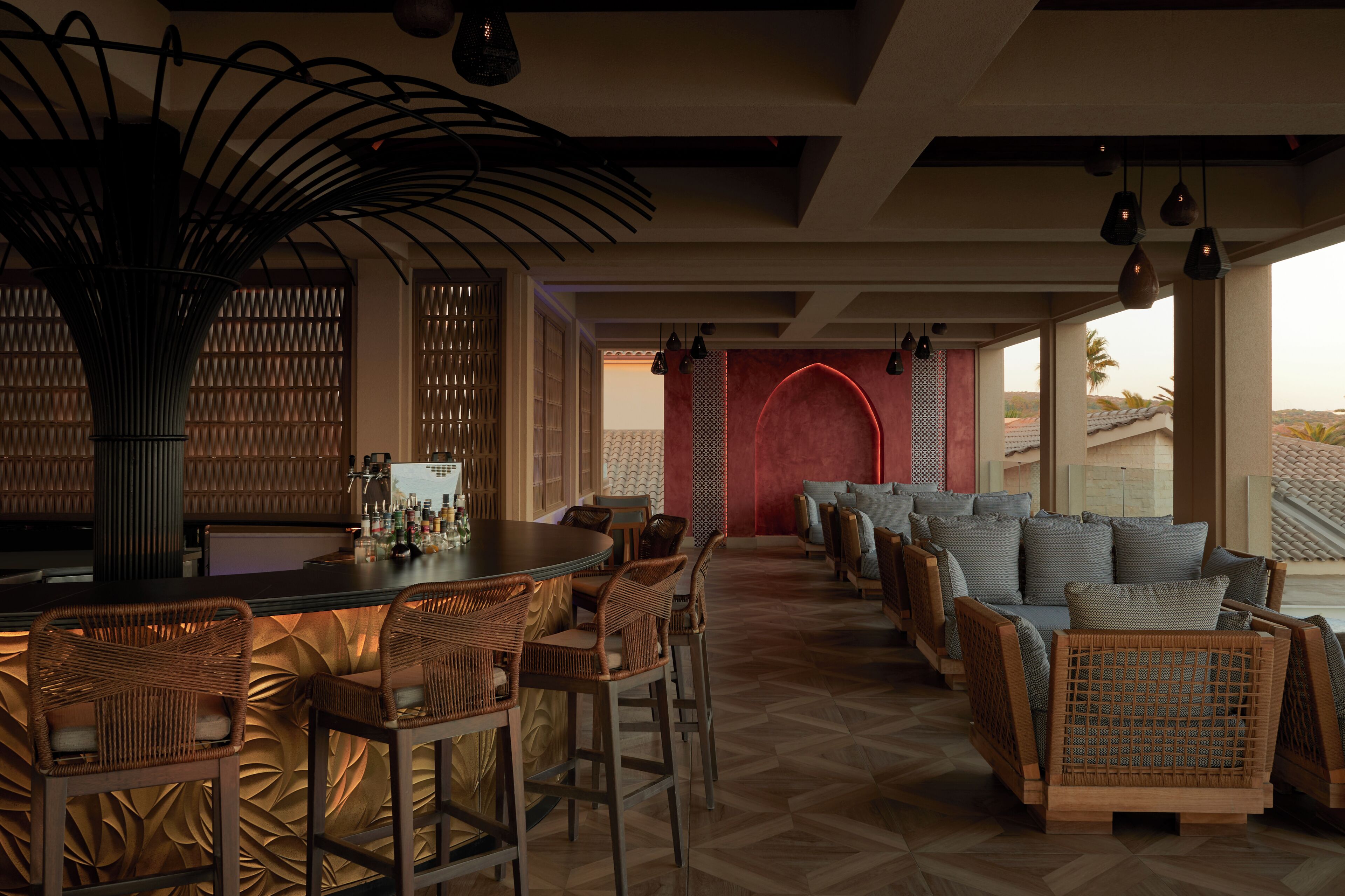 A bar area with wicker furniture, a red accent wall, and a view of palm trees.