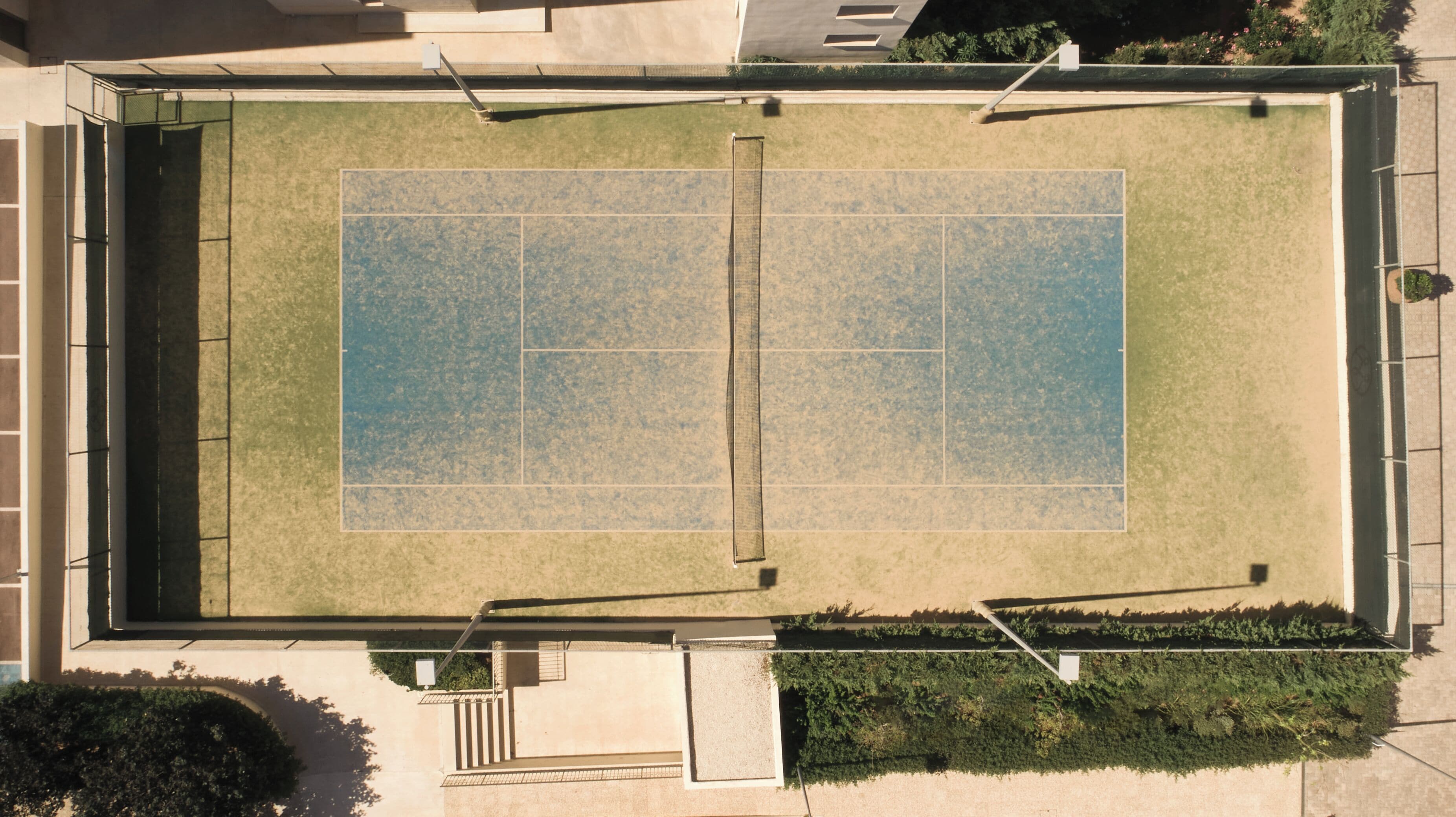 An aerial view of a tennis court with surrounding greenery and a building structure.