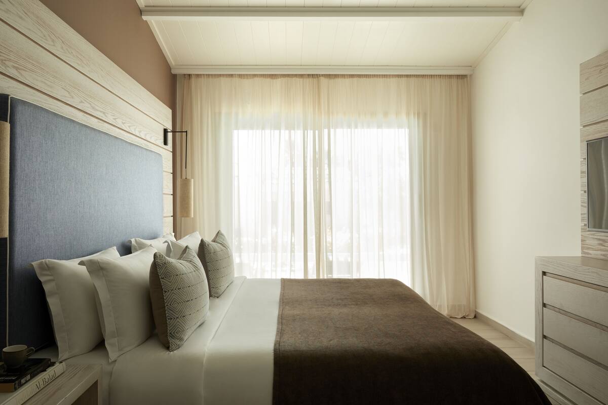 Een netjes opgemaakt slaapkamer met een groot bed, een nachtkastje met boeken en een televisie op een dressoir.