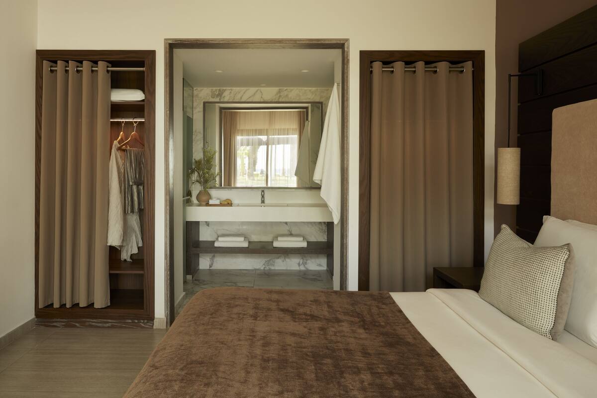 Een hotelkamer met een bed, een badkamer met spiegel, wastafel en kledingkast.