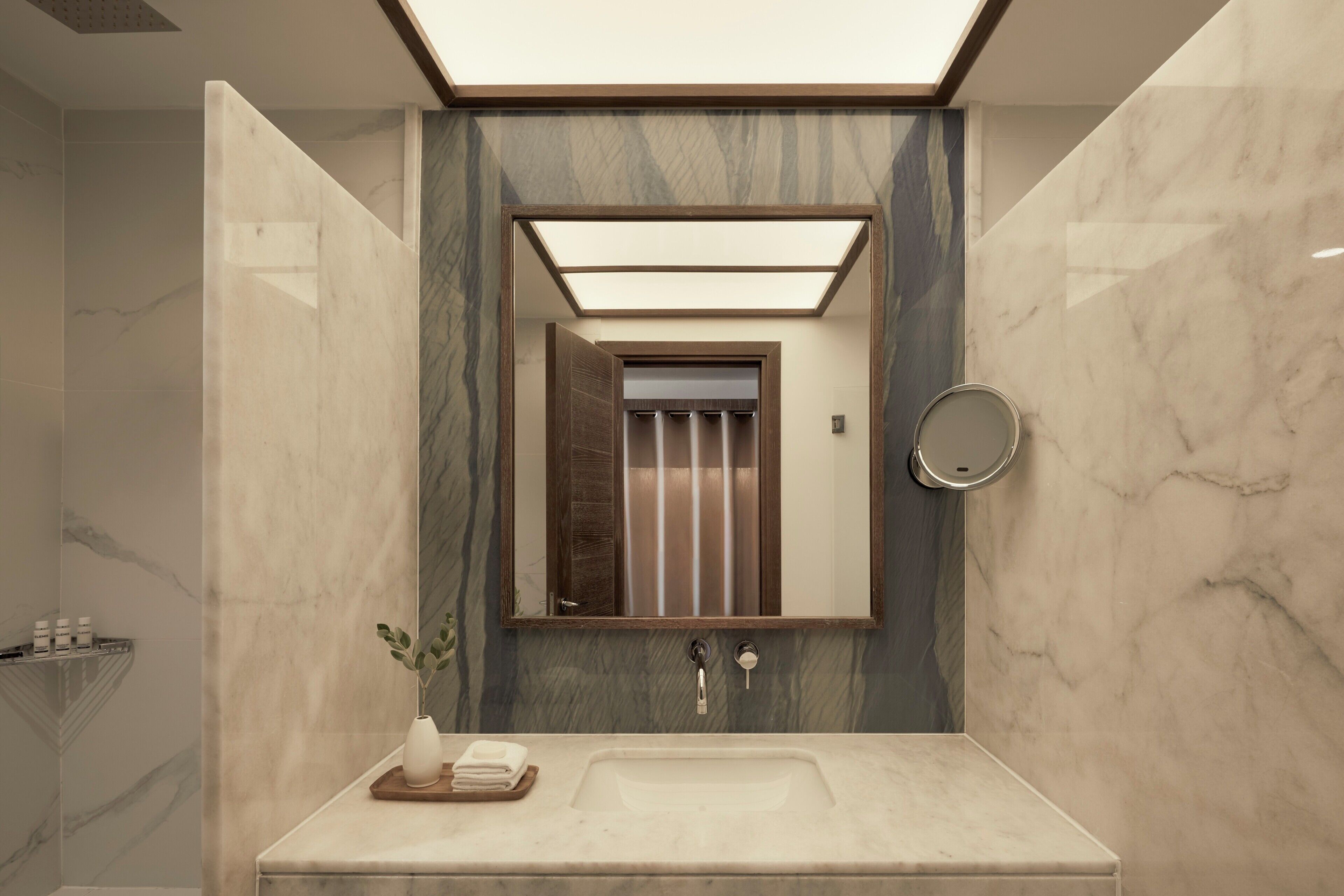 Un baño moderno con tocador de mármol, espejo y zona de ducha.