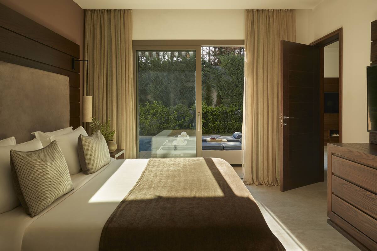 Een slaapkamer met een groot bed, een houten dressoir en een schuifdeur die leidt naar een balkon.