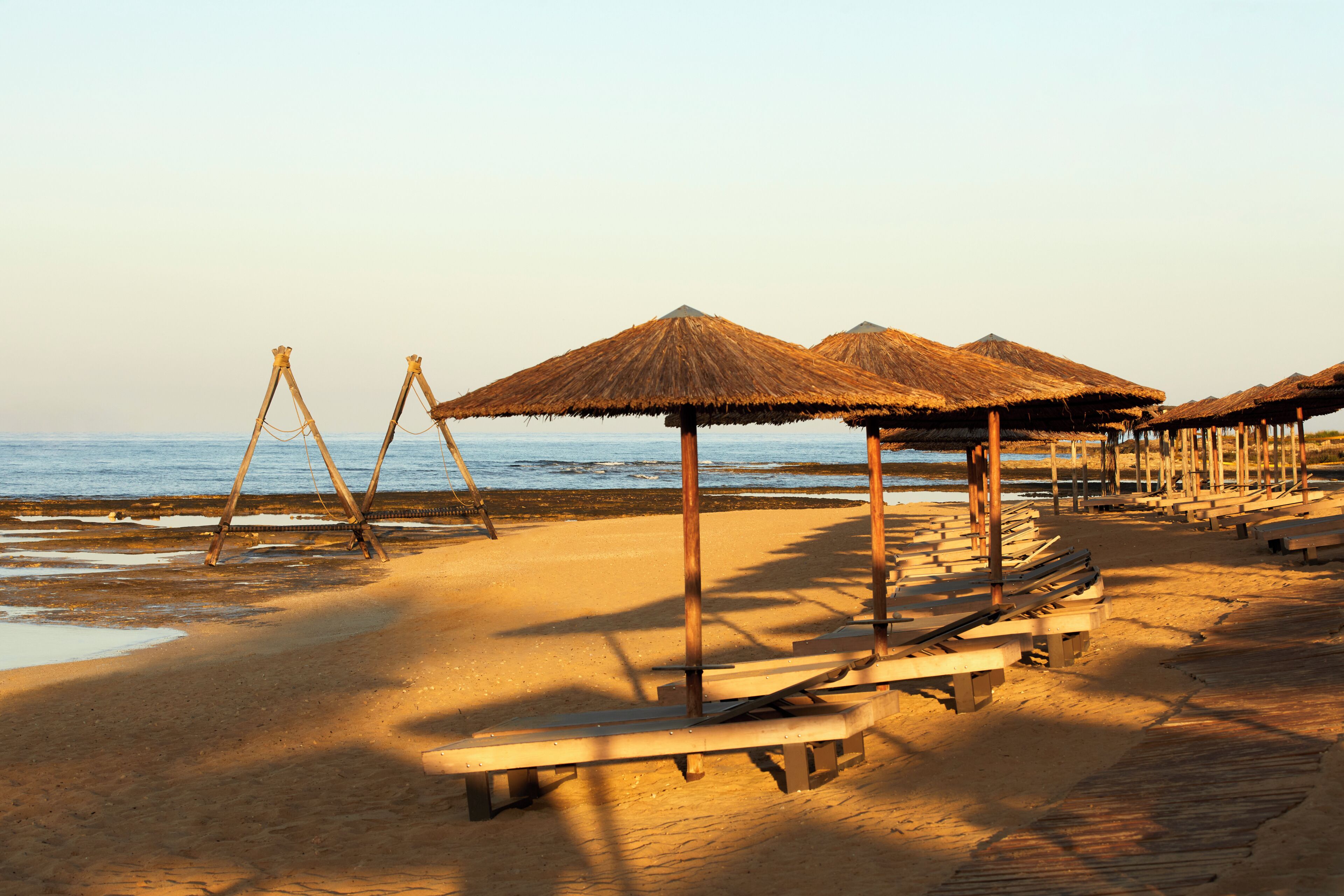 A beach with wooden benches and thatched umbrellas.