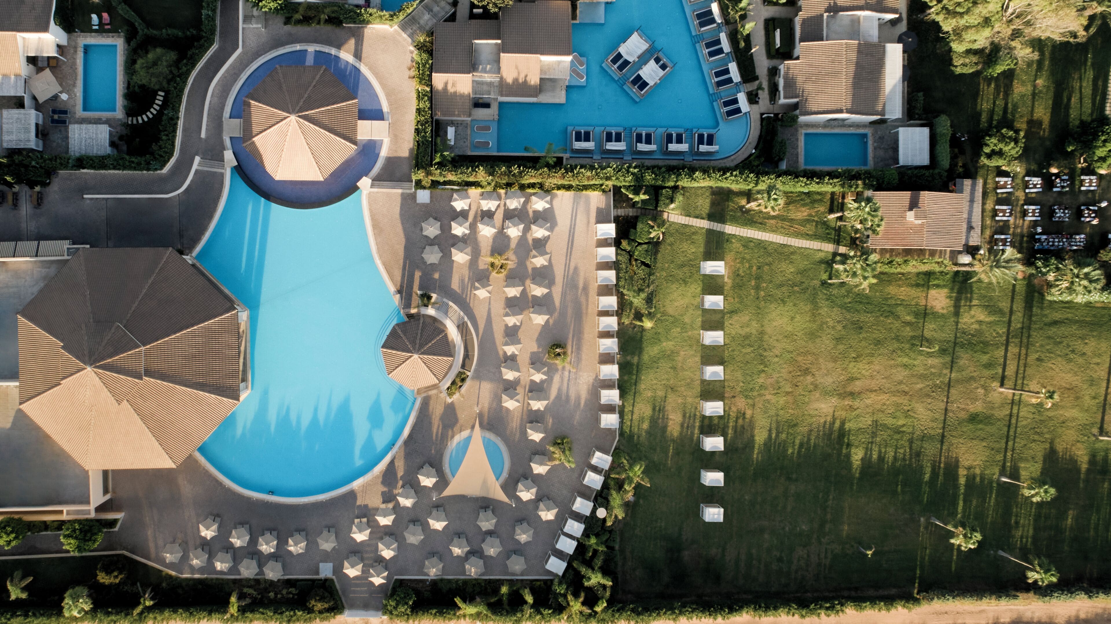 Luchtbeeld van een resort met een centraal gelegen zwembad, ligbedden en een verzorgd gazon.