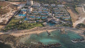 Luchtbeeld van een resort met meerdere gebouwen, een groot zwembad en een strand.