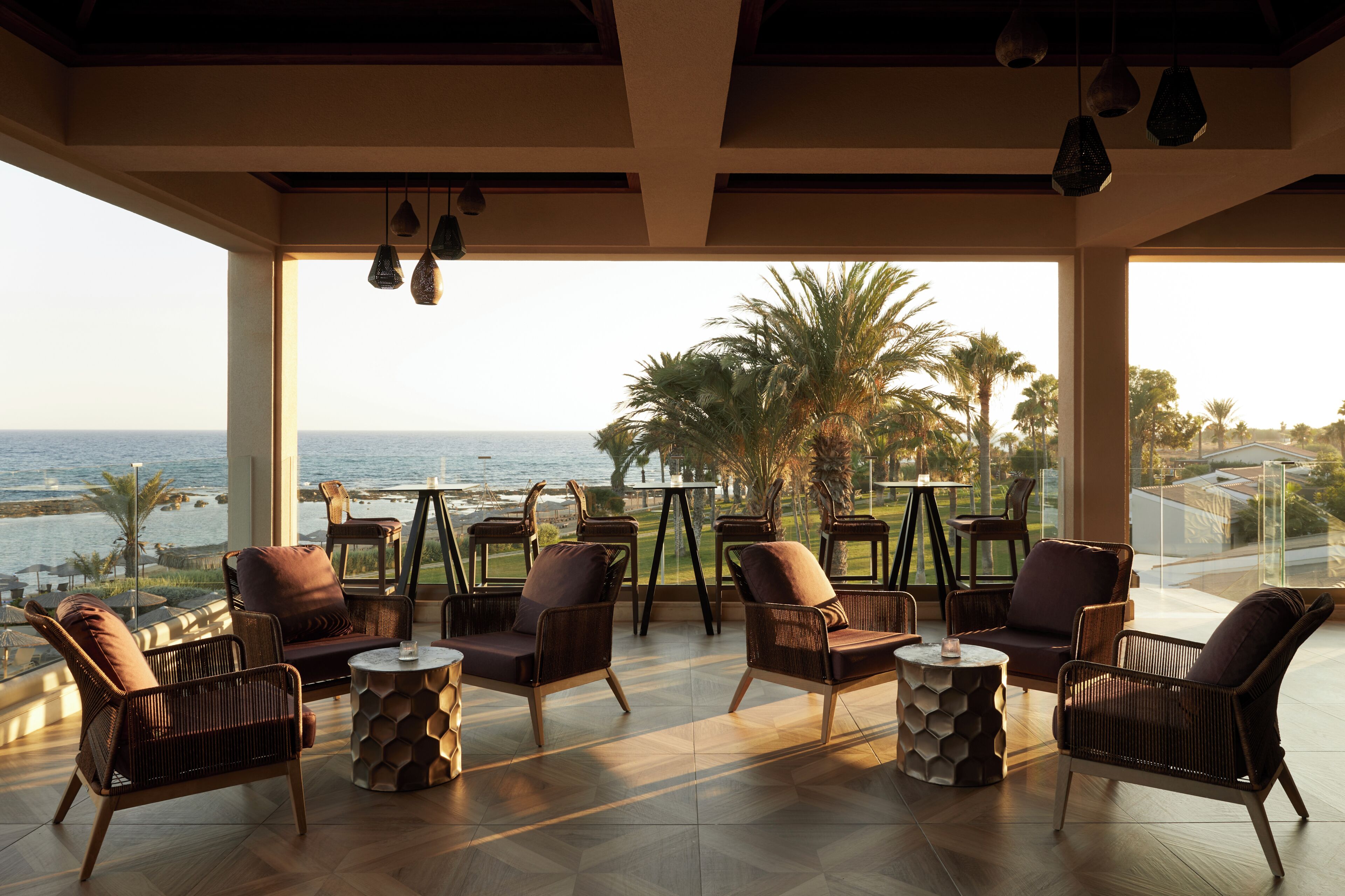 A spacious balcony with wicker furniture, a view of the ocean, and palm trees.