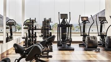 A gym with various exercise equipment, large windows, and a view of the ocean.