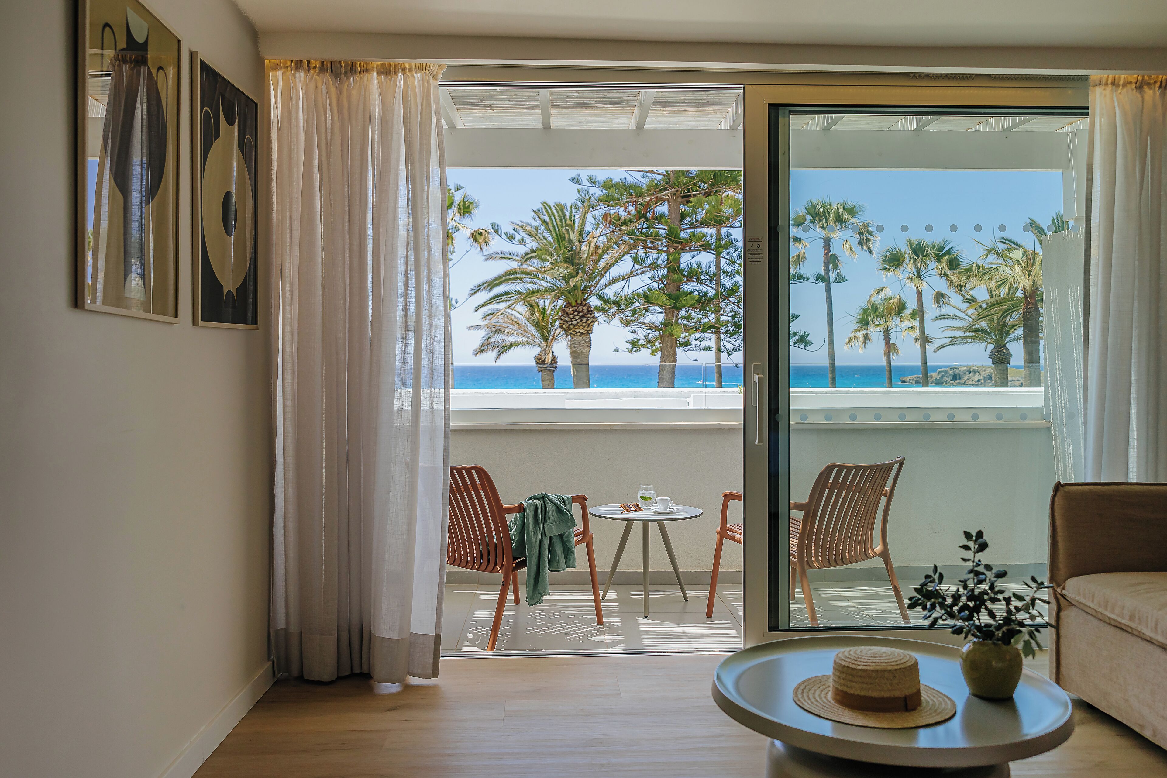 A room with a balcony, a round table with a hat, a chair, and a sofa.