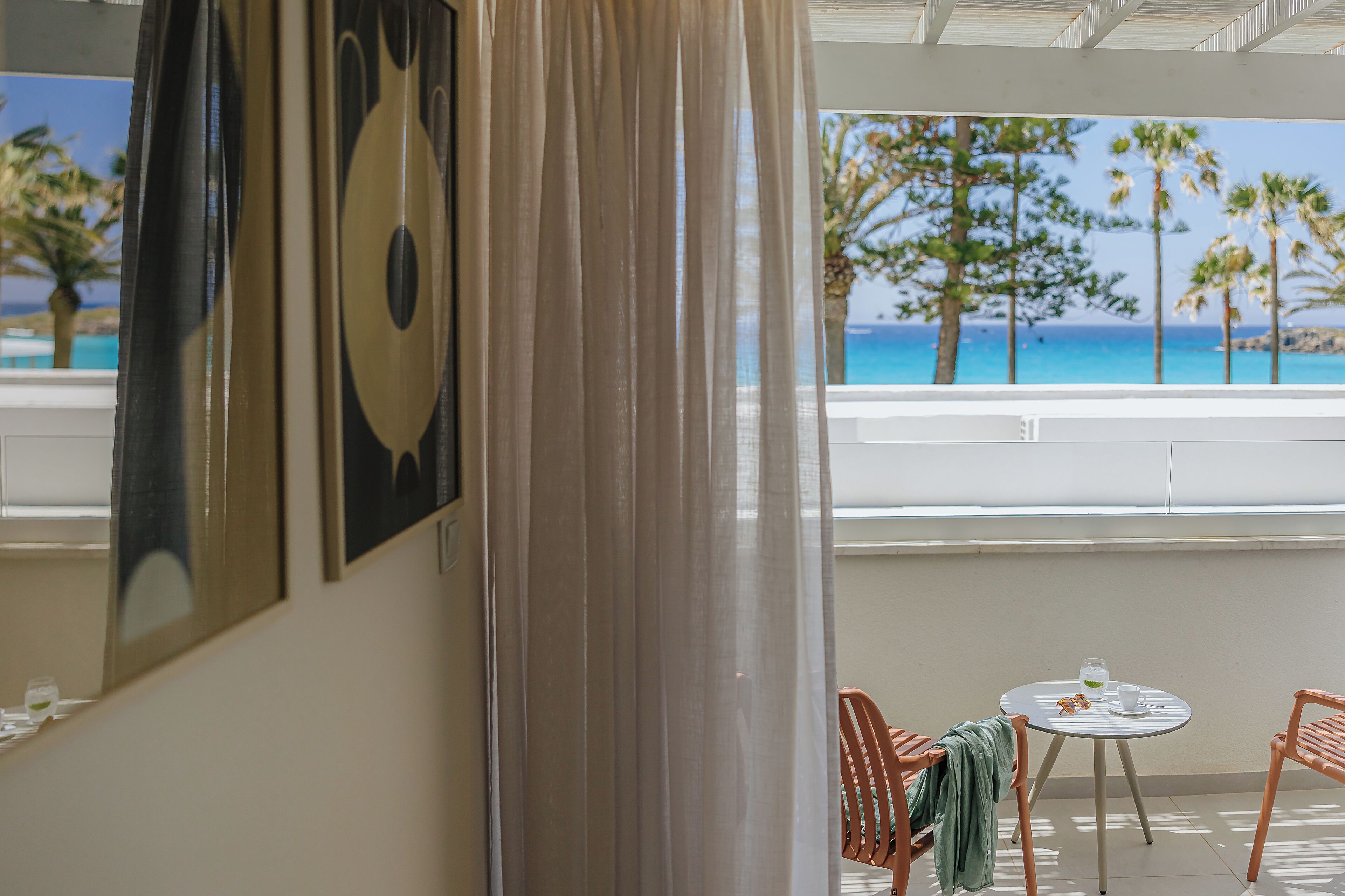 Una habitación con vista al mar, una mesa con sillas y una ventana con cortina.