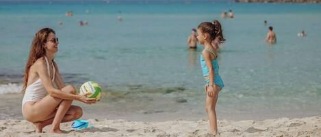A beach scene with a woman and a child playing with a volleyball.