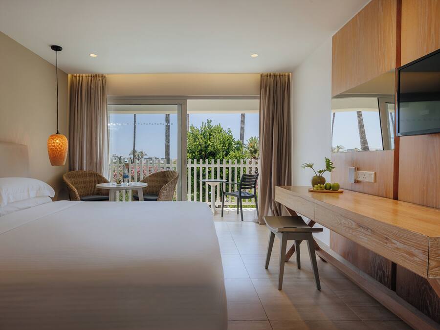 Une chambre d’hôtel avec un lit, une table à manger, des chaises, une télévision et un balcon avec vue.