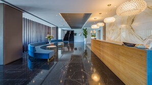 A modern lobby with a curved blue seating area, a wooden reception desk, and a marble wall. - Sun Hall Hotel (Larnaca)