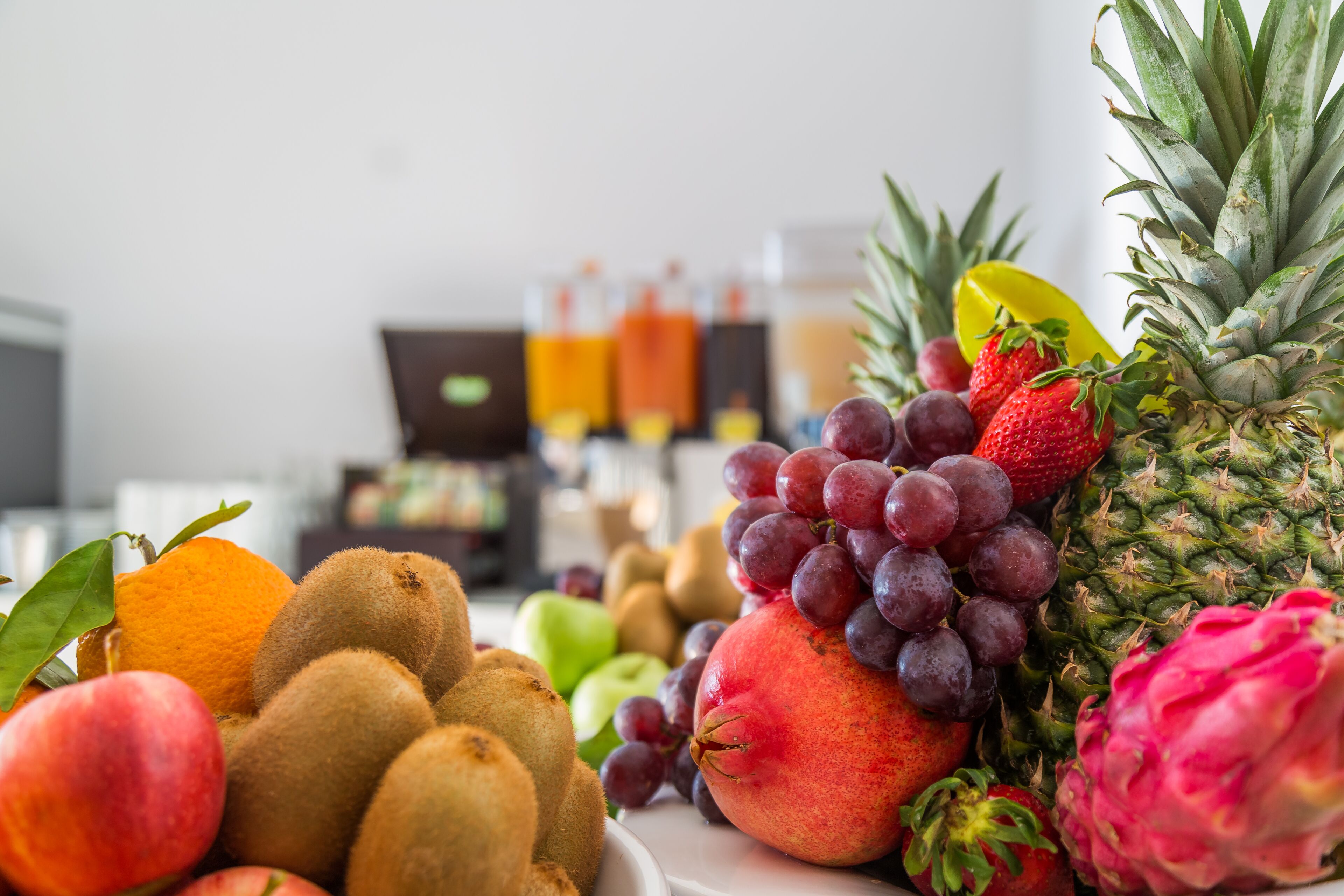 Variedad de frutas, como kiwis, melocotones, uvas, fresas y una pitahaya, sobre una mesa.