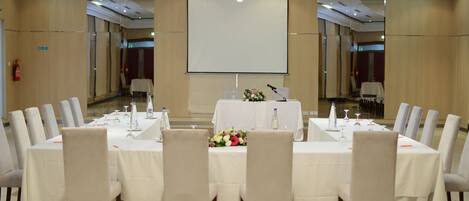 A conference room with a long table, chairs, a projector screen, and a chandelier.
