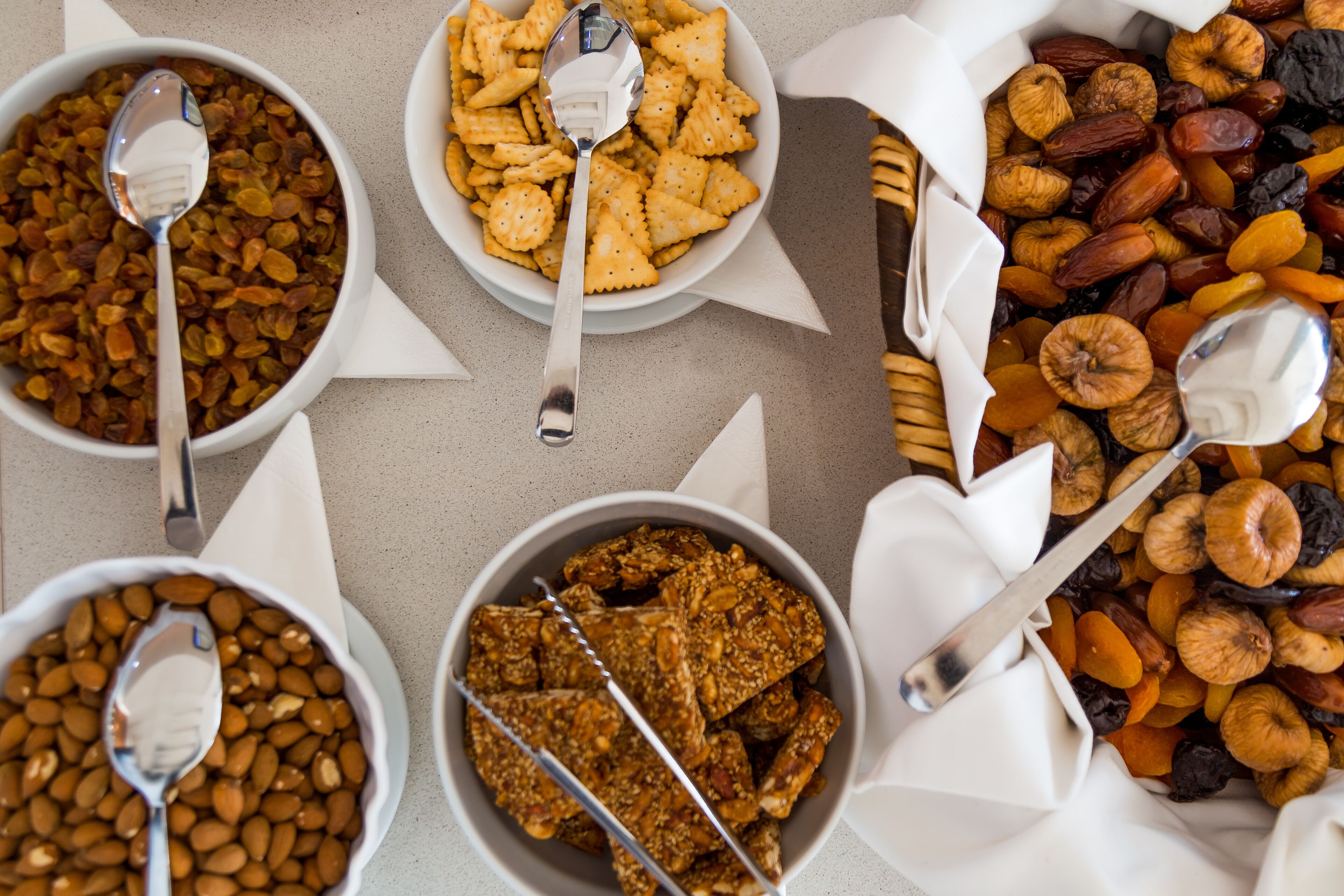 Four bowls of snacks with spoons, arranged on a table.