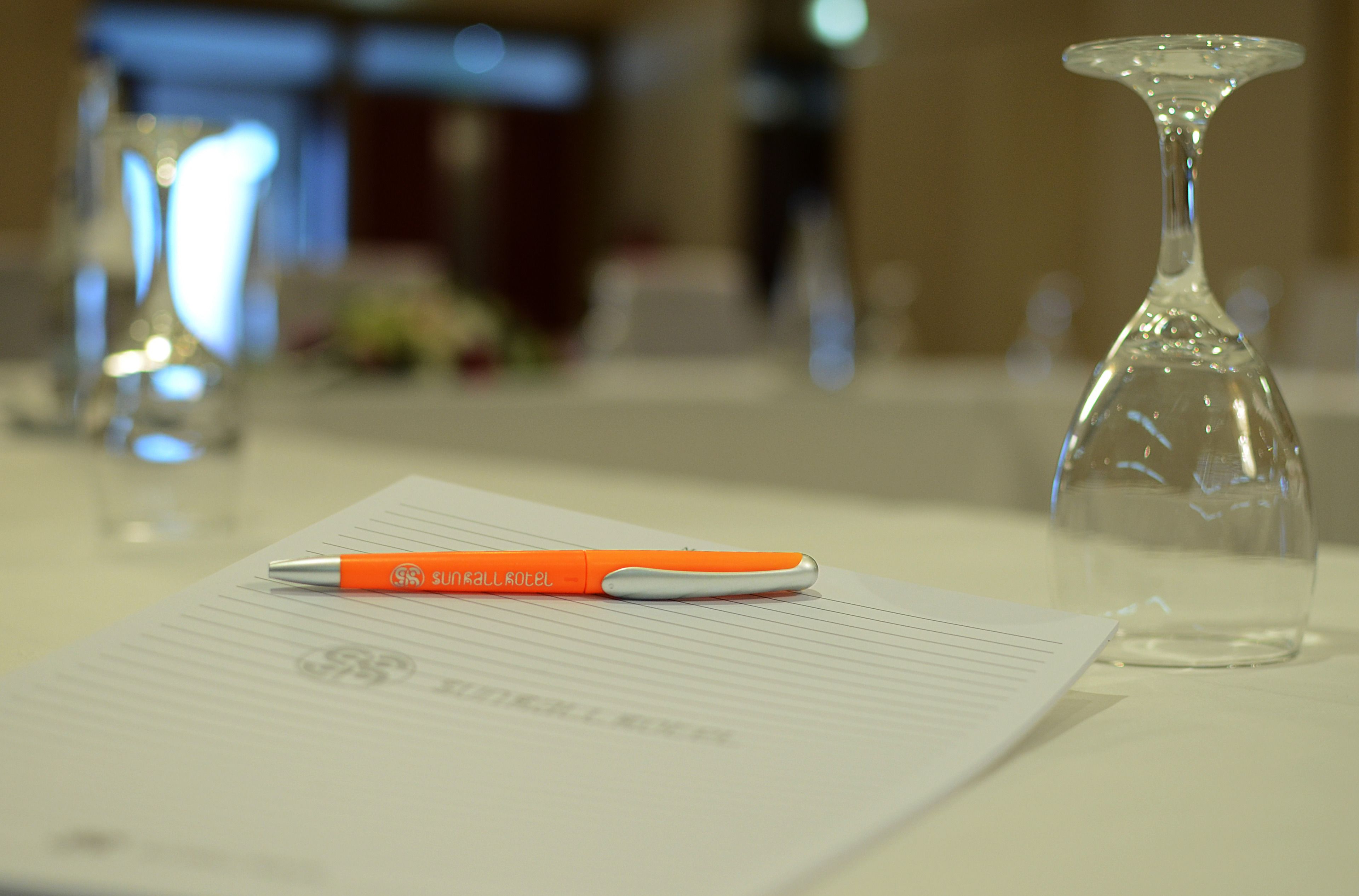 A pen on a piece of paper with a watermark, a clear glass vase, and a blurred background.