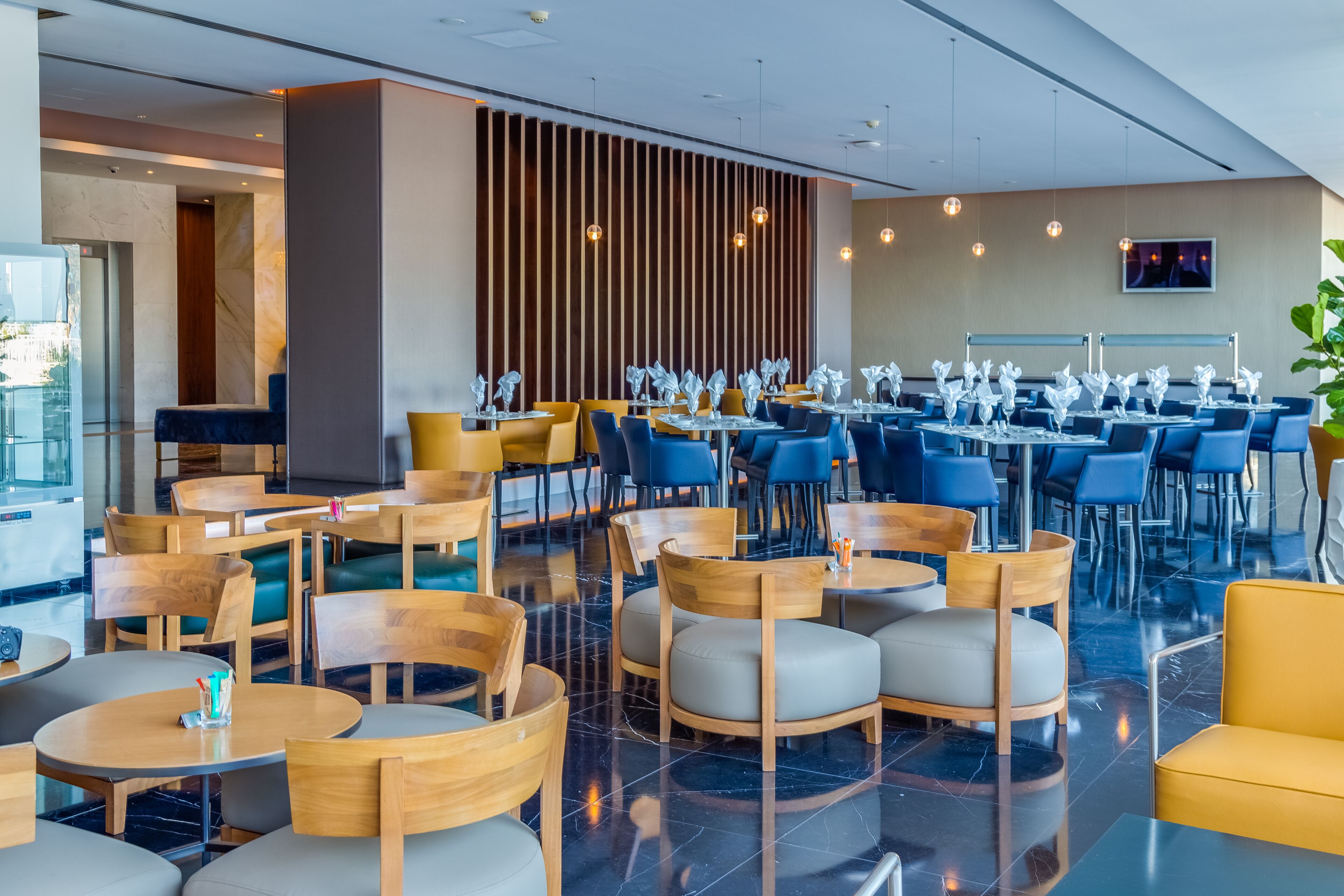 A modern restaurant with wooden and blue chairs, tables, and a decorative wall.