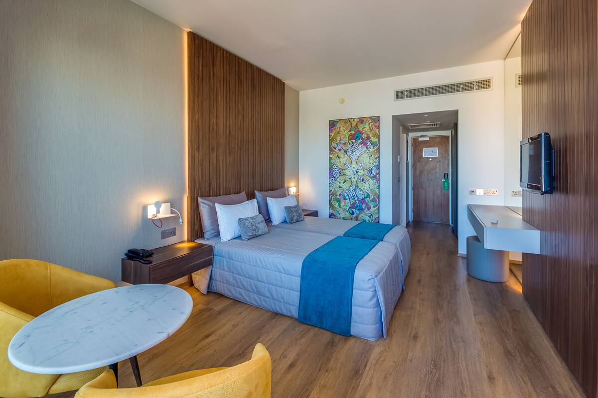 A hotel room with a bed, bedside tables, a desk, a chair, a TV, and a bathroom.