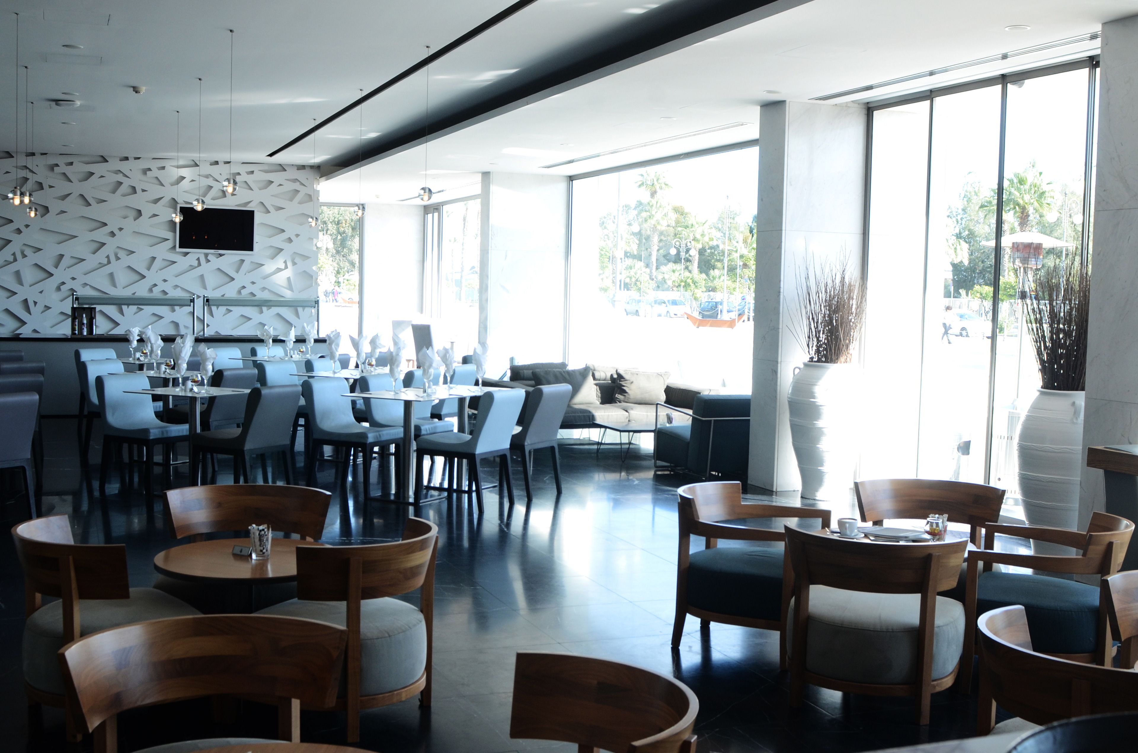 A modern restaurant with a geometric wall design, multiple seating areas, and large windows offering a view of the outdoors.