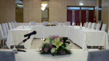 A conference room with a long table, chairs, microphones, and a floral centerpiece.