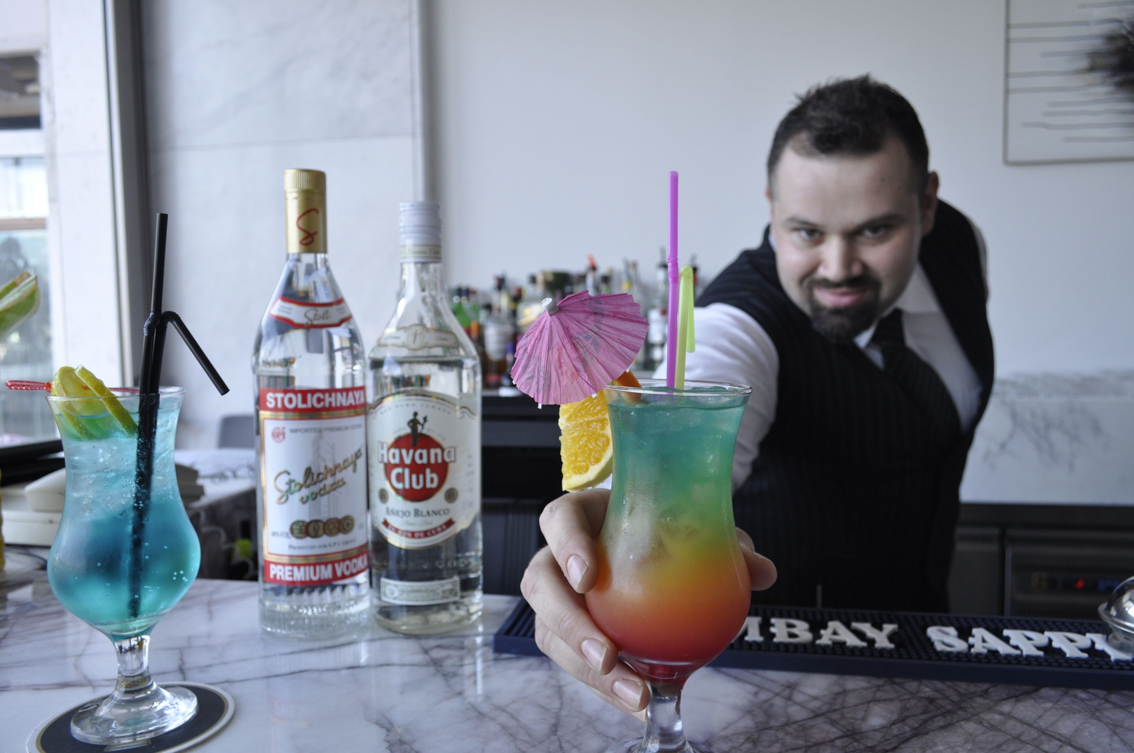 A bar area with two cocktails, a bottle of Stolichnaya vodka, and a keyboard with "BAY SAPPHIRE" on it.