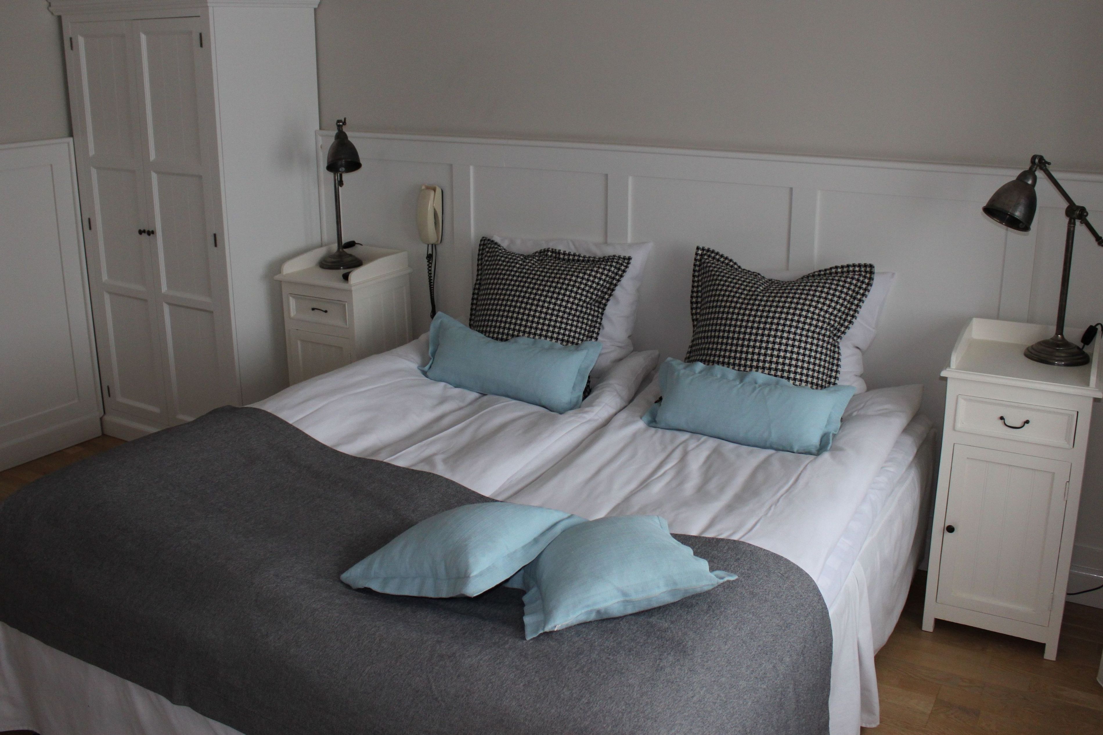 A neatly made bed with white bedding and two blue pillows, flanked by white nightstands with lamps.