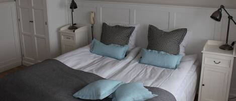 A neatly made bed with white bedding and two blue pillows, flanked by white nightstands with lamps.