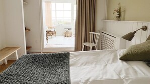 A bedroom with a bed, a chair, a small table, a radiator, and a window with curtains. - Hjerting Badehotel - Esbjerg (Esbjerg)