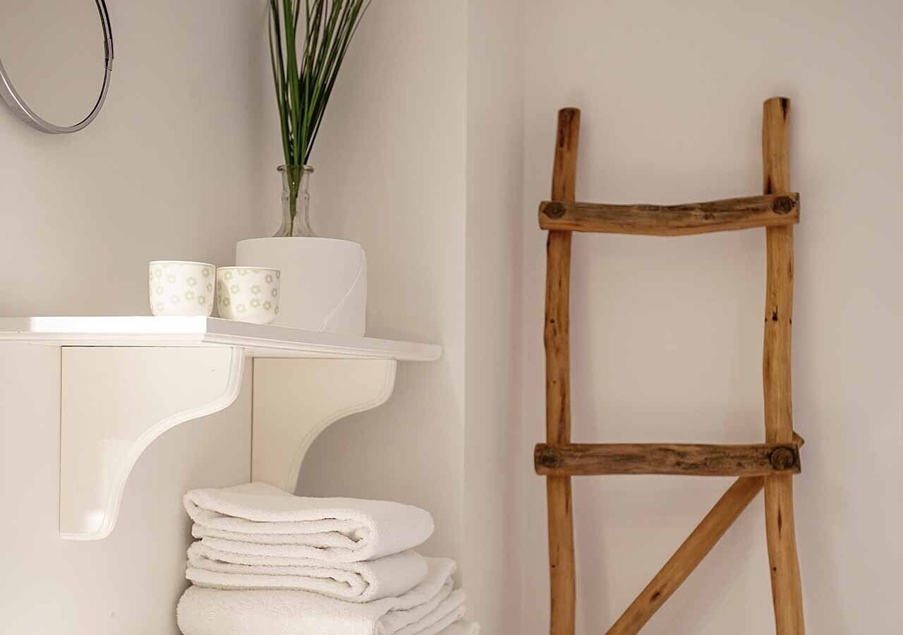 A bathroom with a white sink, a wooden ladder, and a stack of towels.