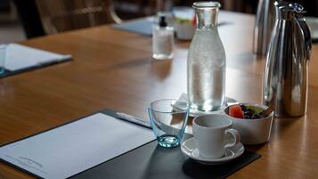 A wooden table with a water bottle, a coffee pot, a cup, and a bowl of fruit.