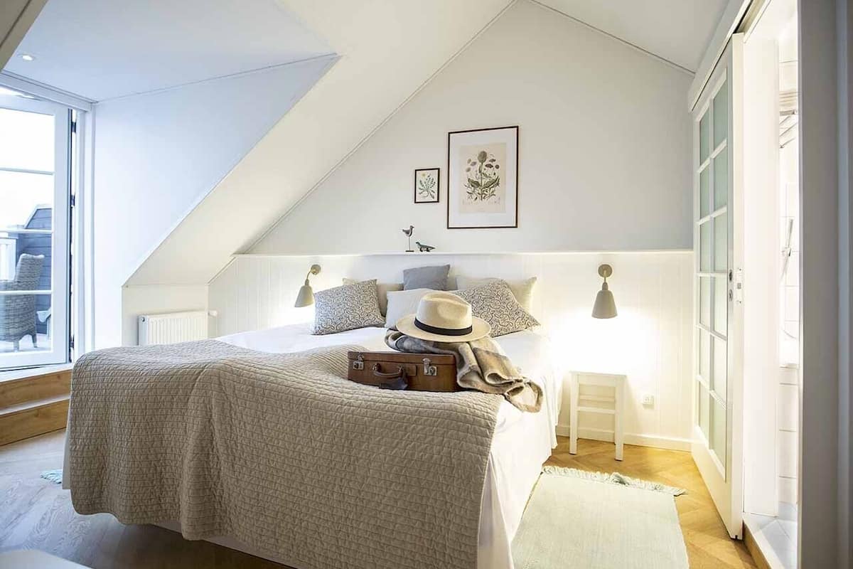 Une chambre à coucher avec un lit, une valise, un chapeau et une petite table avec une lampe.