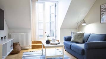 En moderne stue med en blå sofa, et hvidt sofabord og et stort vindue med gardiner.