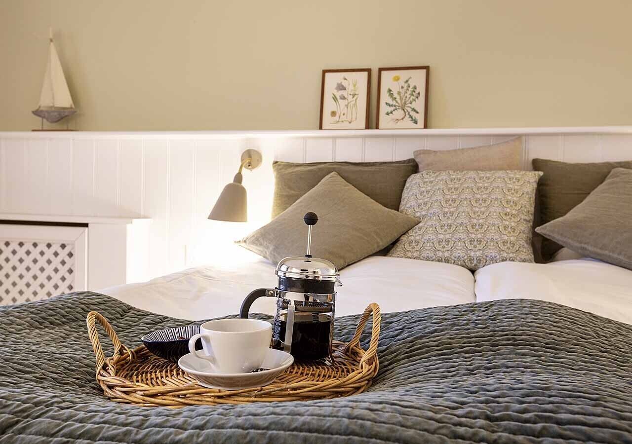 En pænt redt seng med kaffemaskine, kop og bakke på et vamset tæppe.