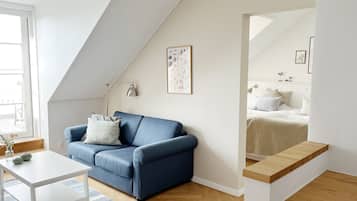 Un dormitorio estilo loft moderno con techo inclinado, un sofá azul, un escritorio blanco y un espejo grande.