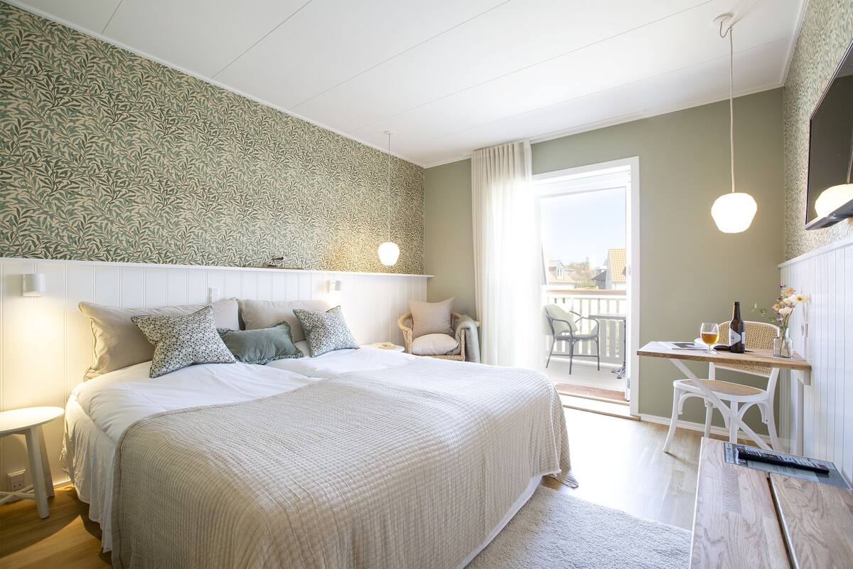 Une chambre avec un grand lit, une petite table sur laquelle se trouvent une bouteille et un verre, et une chaise.