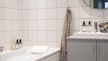 A modern bathroom with a white bathtub, a vanity with a mirror, and toiletries on the counter.