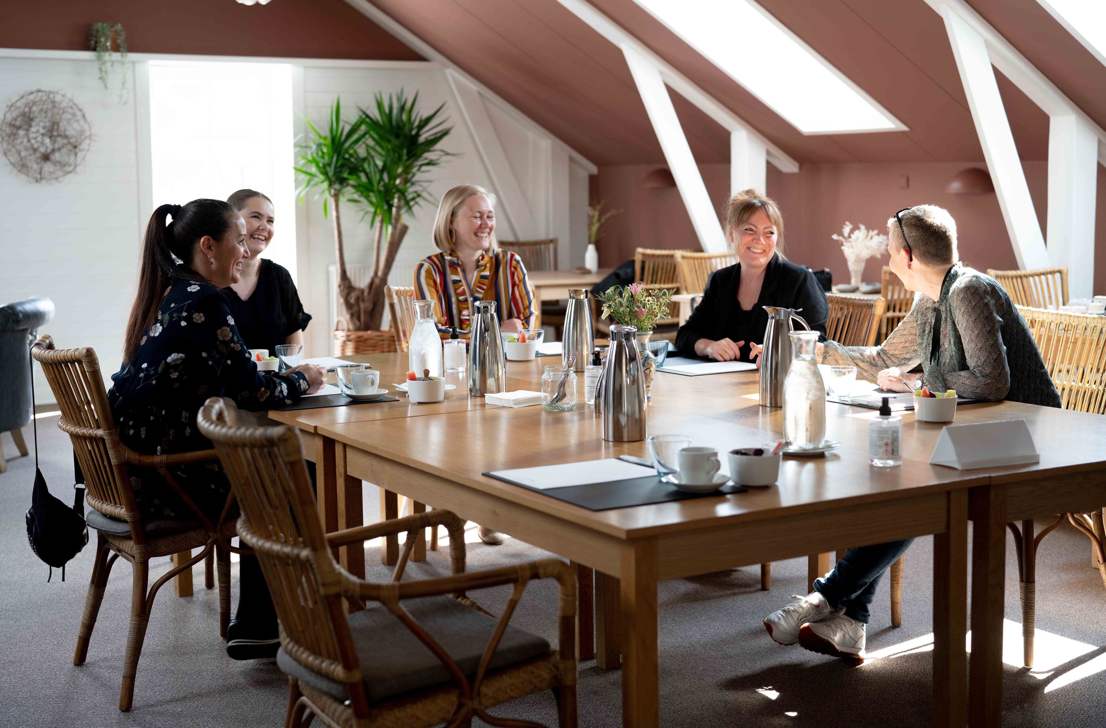 A group of people seated around a wooden table in a room with high ceilings and natural light.