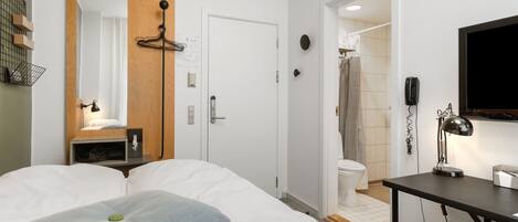 A hotel room with a bed, a desk, a mirror, a wooden panel, a shower area, and a toilet.